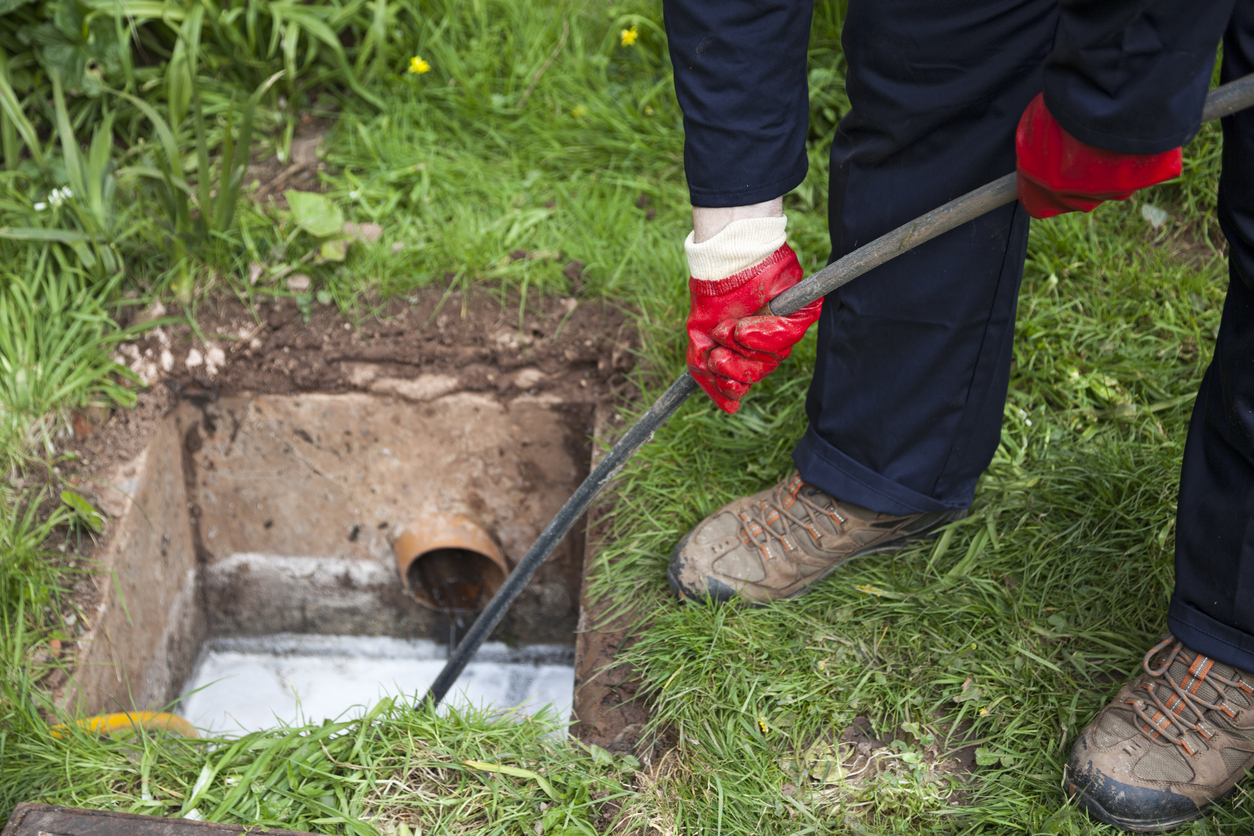 Drain being cleared by worker in navy overalls.